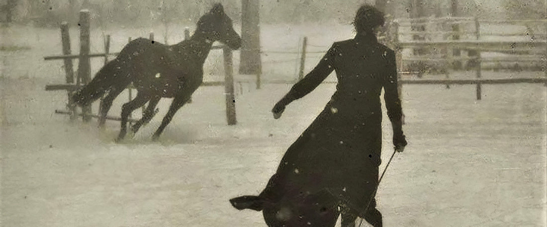 A woman in a long coat walking away across a snow-covered paddock, a dark horse galloping behind her — photograph attributed to Félix Thiollier, 1899