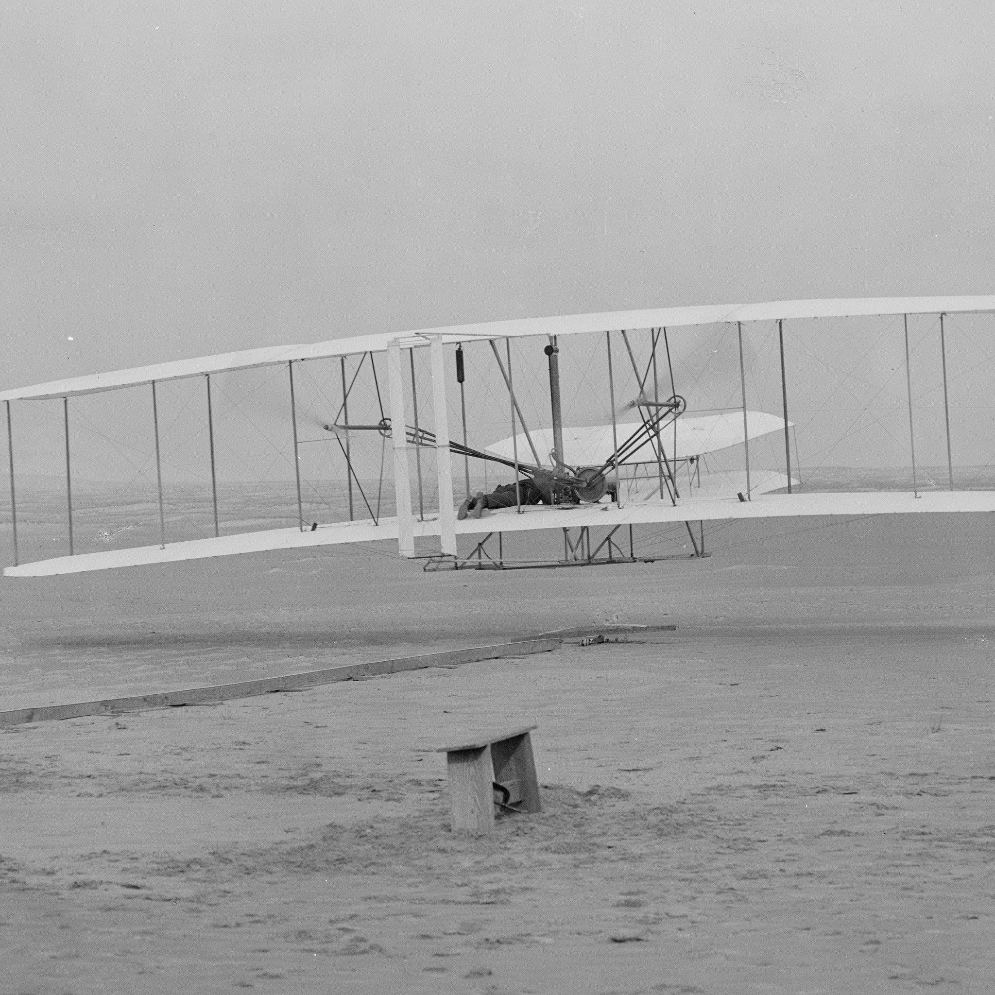 Detail at actual print size: Orville lying at the controls, the launching rail behind the machine and the grain of the 1903 dry plate